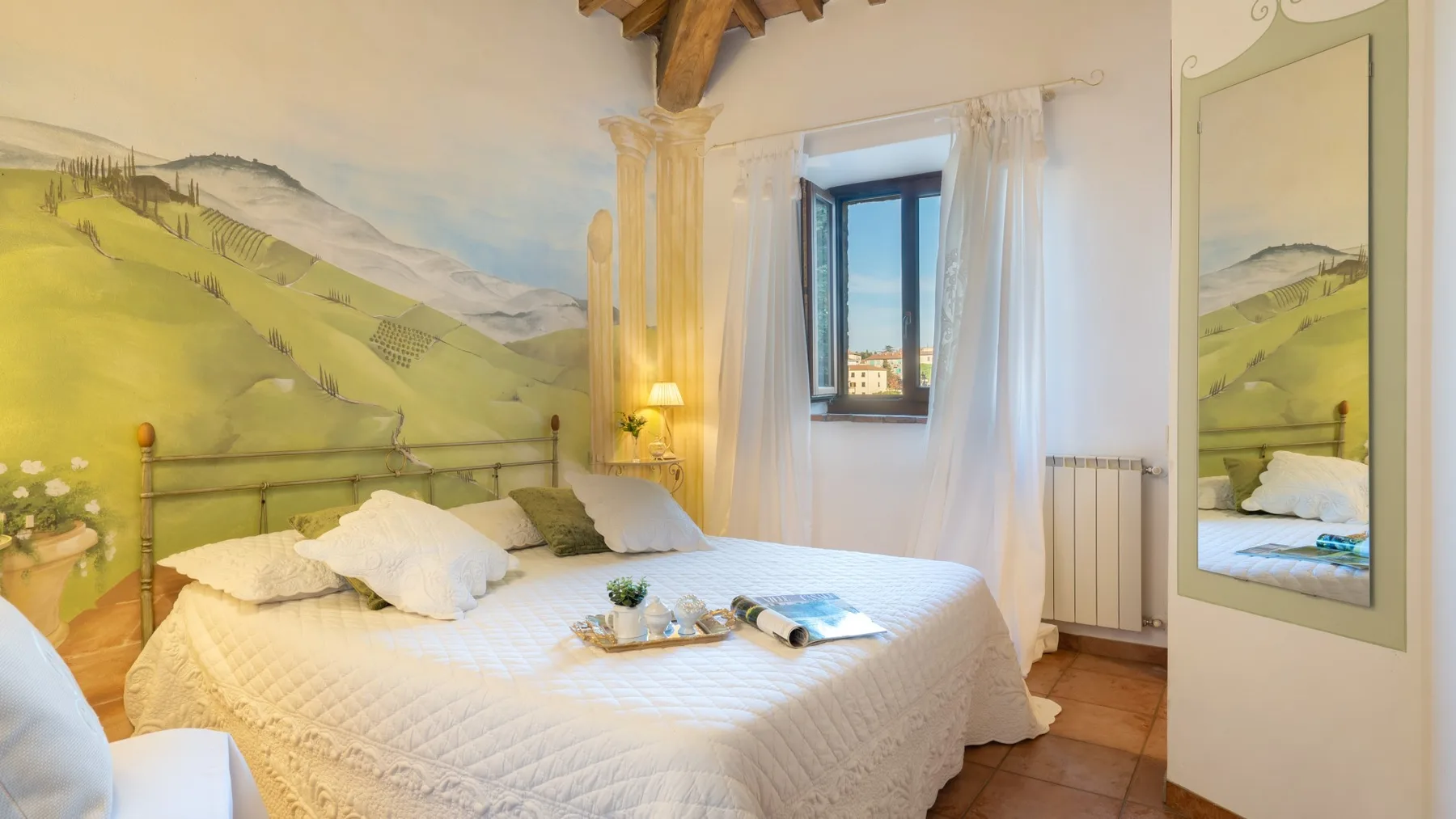 Un dormitorio con una cama bajo un mural pintado de colinas y una ventana.