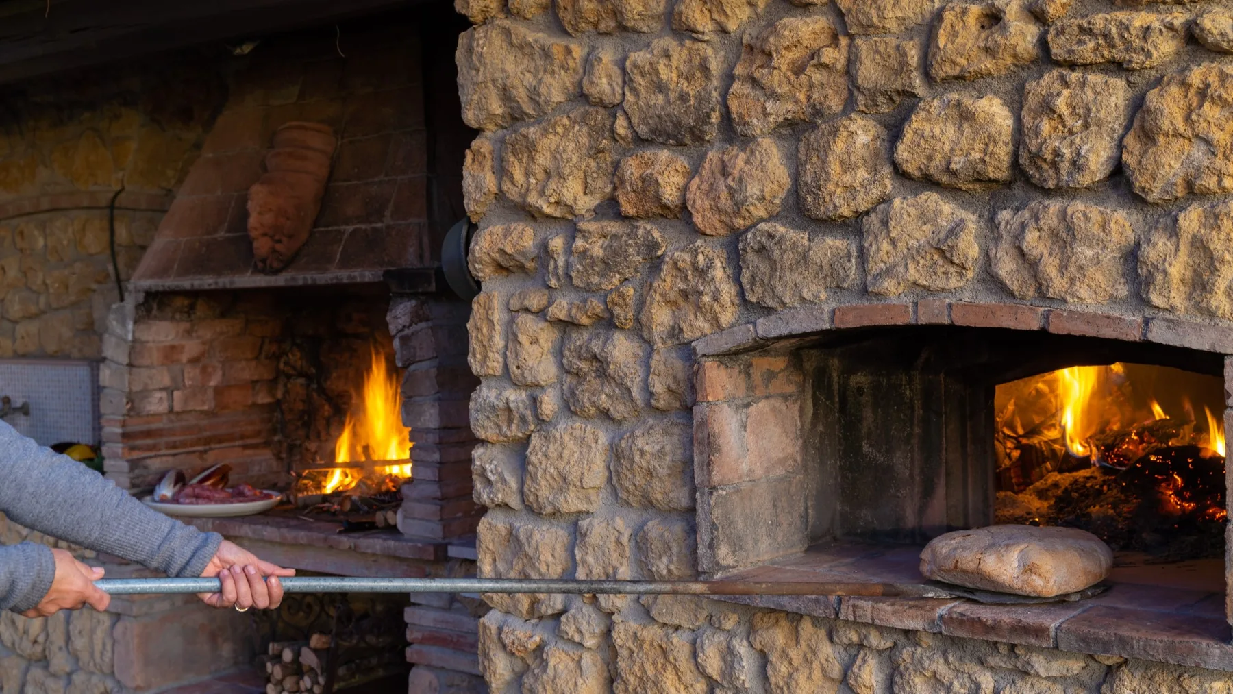 Una chimenea de piedra con leña encendida junto a un horno de ladrillo.