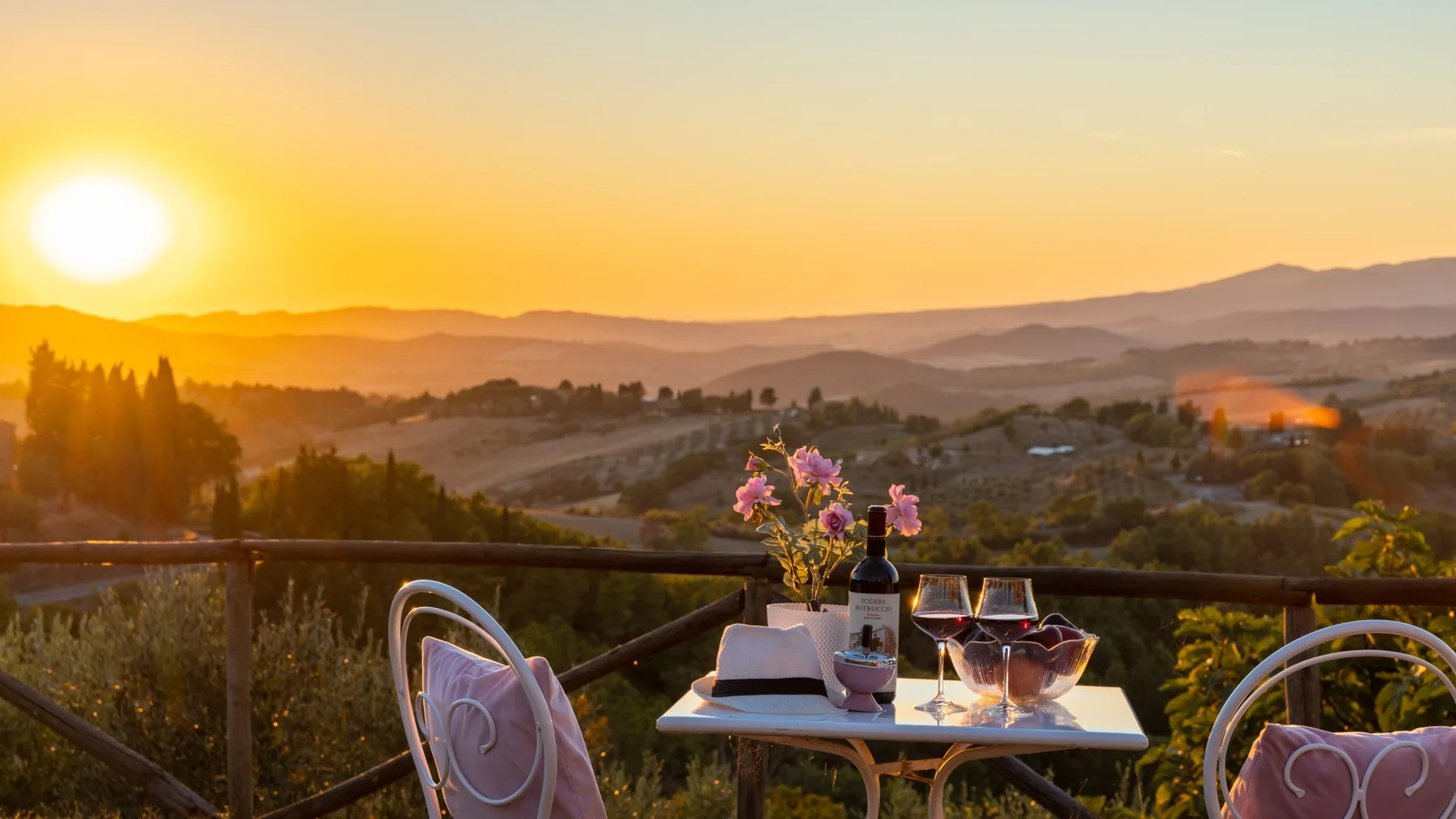 Una mesa de balcón con bebidas tiene vistas a colinas onduladas al atardecer.