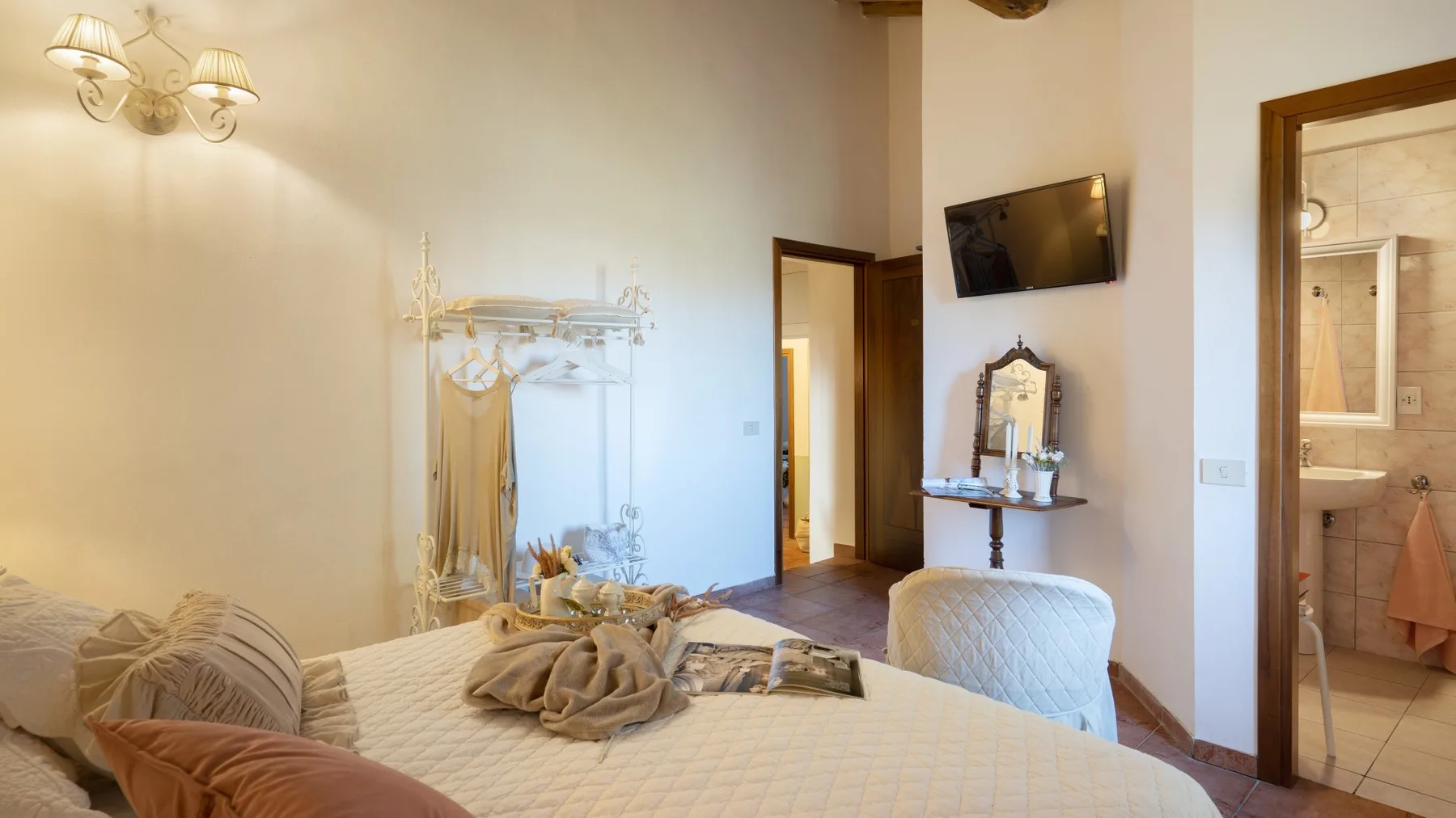 Un dormitorio con una cama, un televisor en la pared y una puerta abierta a un baño.