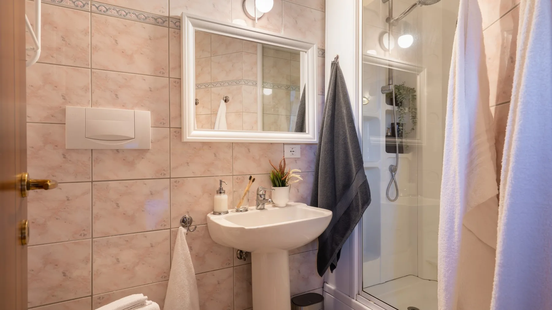 Un baño con azulejos, lavabo de pared, espejo y ducha.