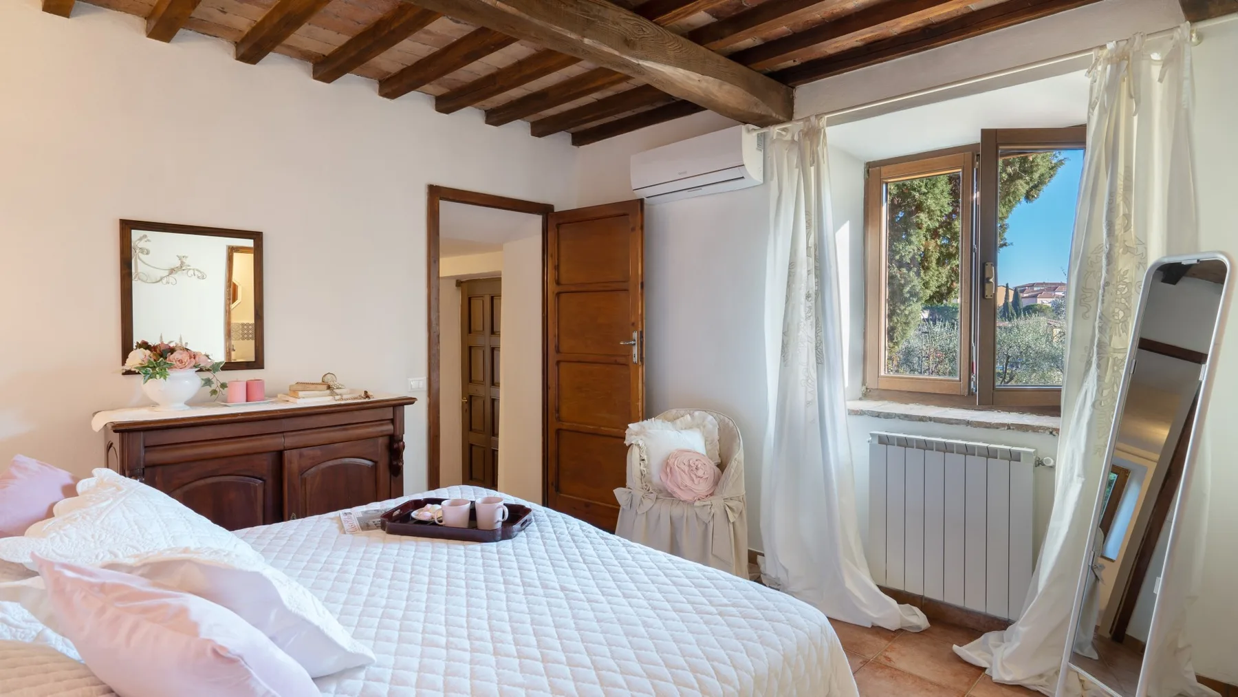 Un dormitorio con una cama acolchada, muebles de madera y una ventana con vistas a la vegetación.