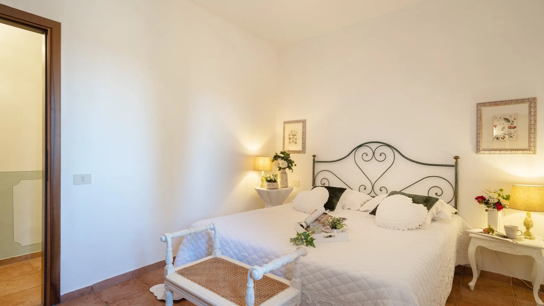 Un dormitorio luminoso con una cama blanca, cabecero de metal decorativo y mesitas de noche.