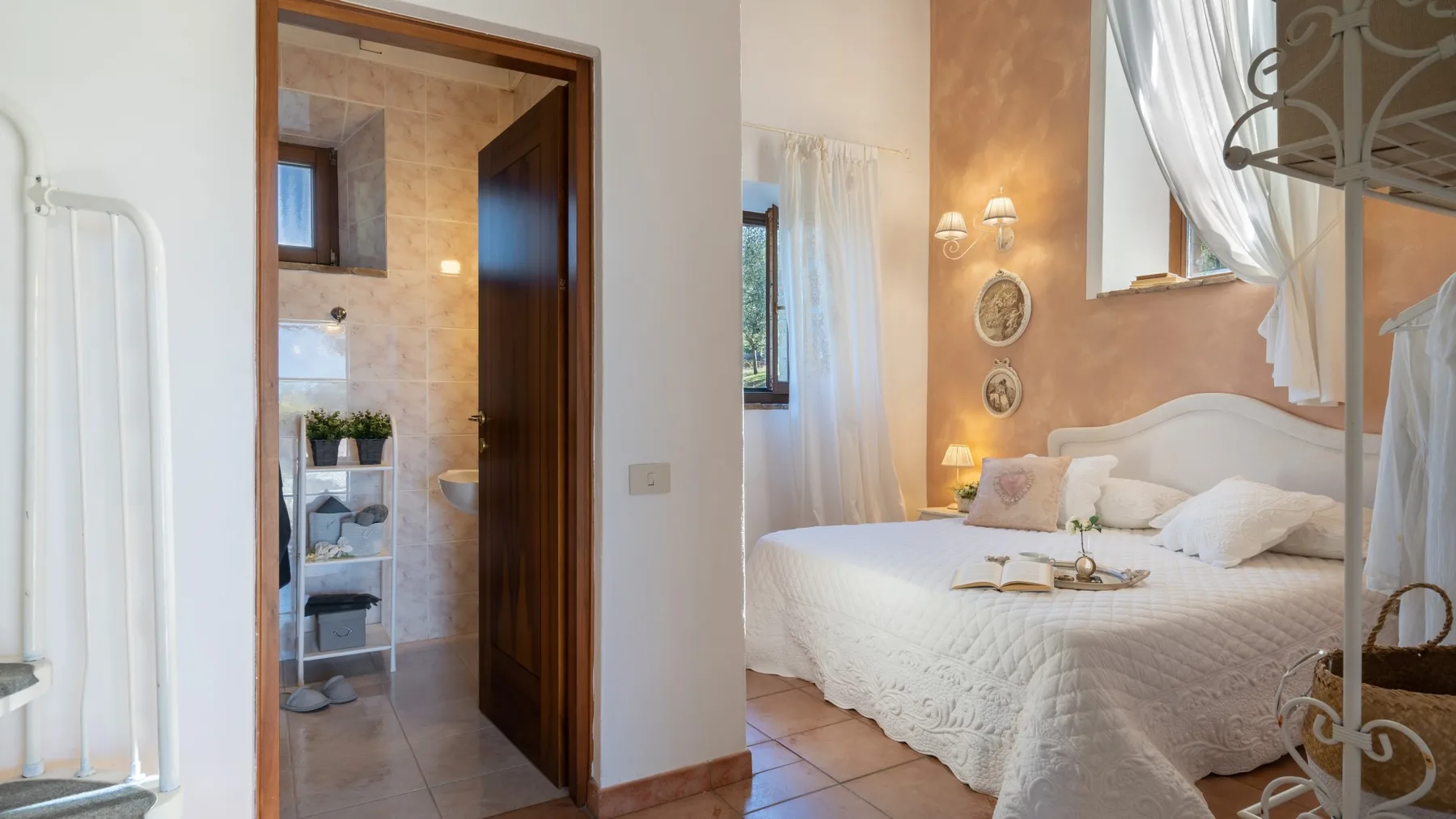 Un dormitorio con una cama bien tendida junto a una puerta abierta a un baño con azulejos.