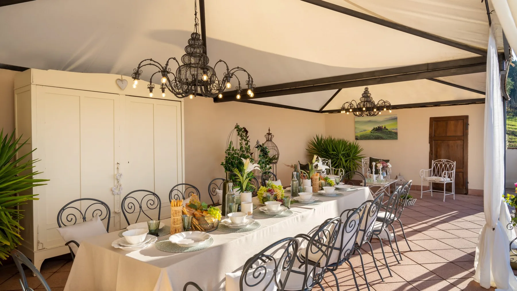 Un comedor cubierto tiene una mesa larga preparada con platos y rodeada de sillas.