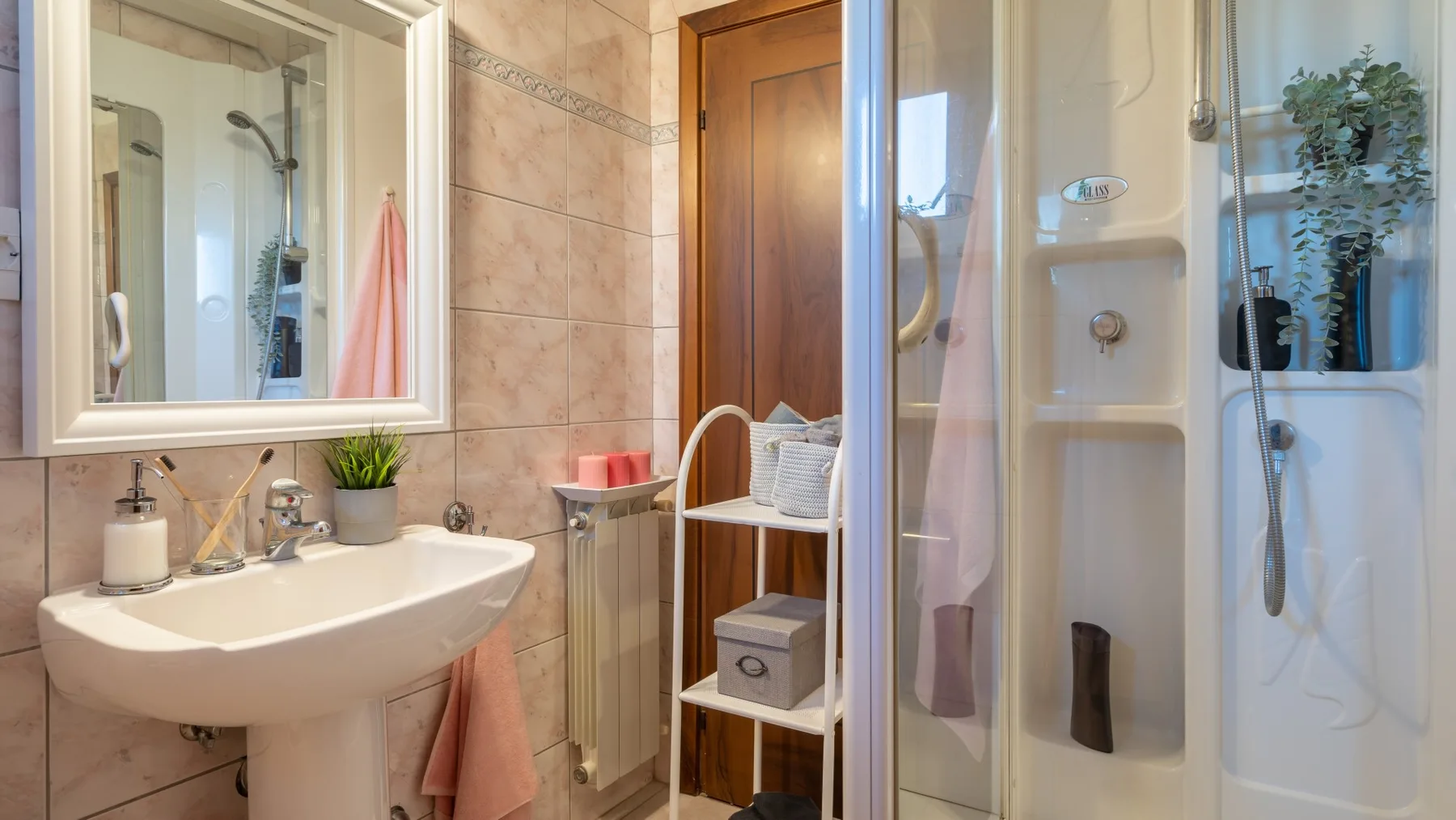 Un baño luminoso con lavabo de pedestal, ducha y una pequeña estantería.