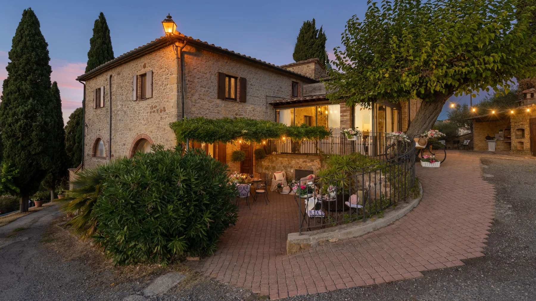 Una casa de piedra con patio de ladrillo y asientos al aire libre al anochecer.