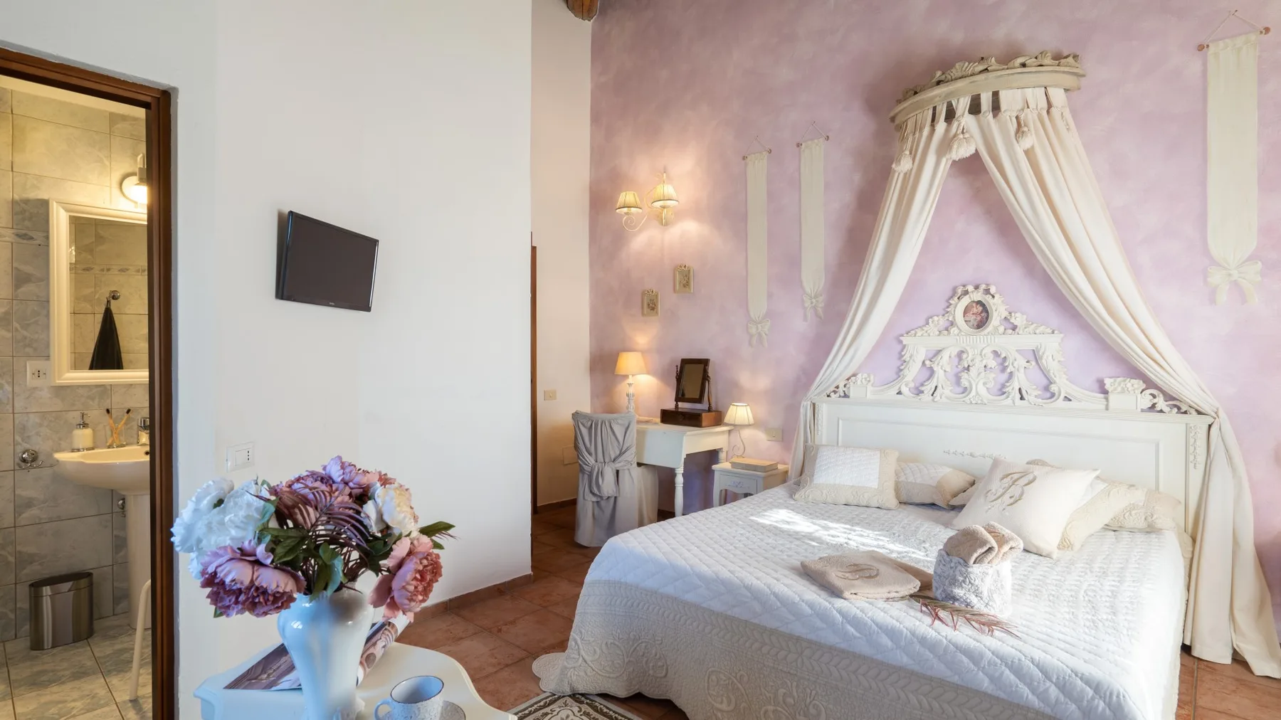 Un dormitorio con una cama con dosel y un arreglo floral sobre una mesa cercana.