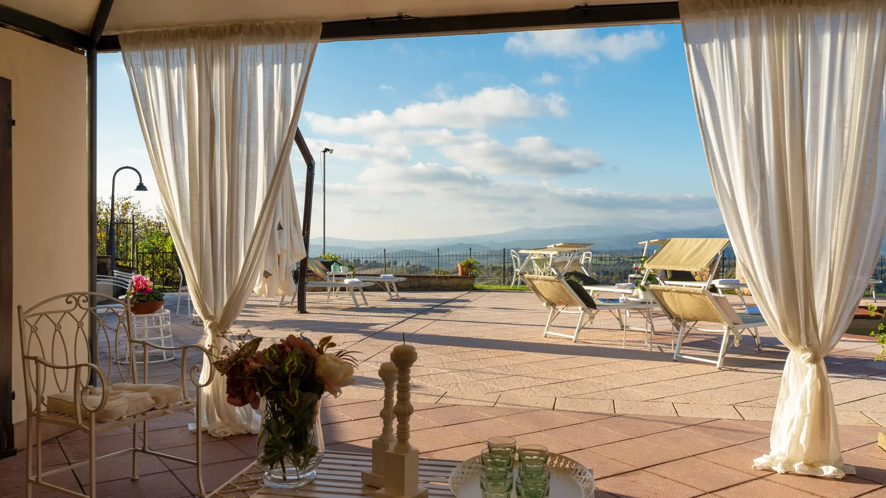 Una terraza exterior cubierta con asientos y cortinas da a un amplio paisaje.