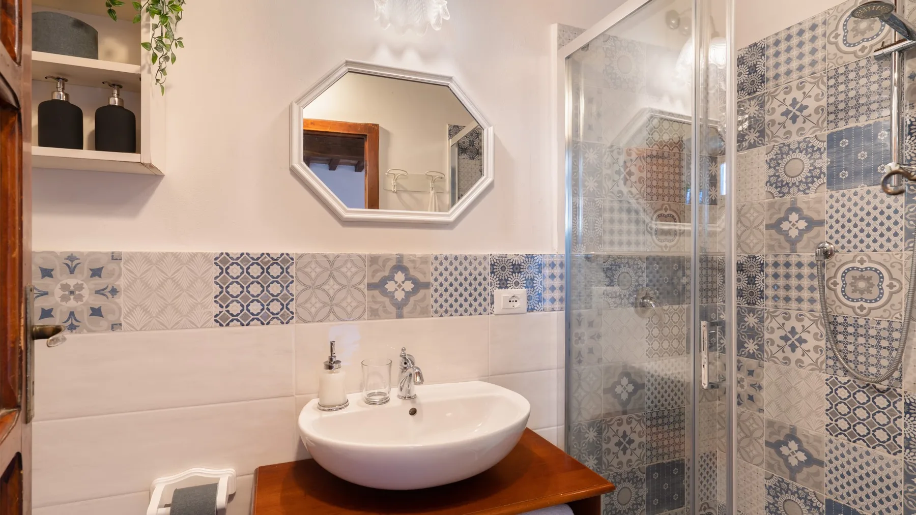Un baño revestido con azulejos, lavabo sobre encimera, espejo y ducha de vidrio.