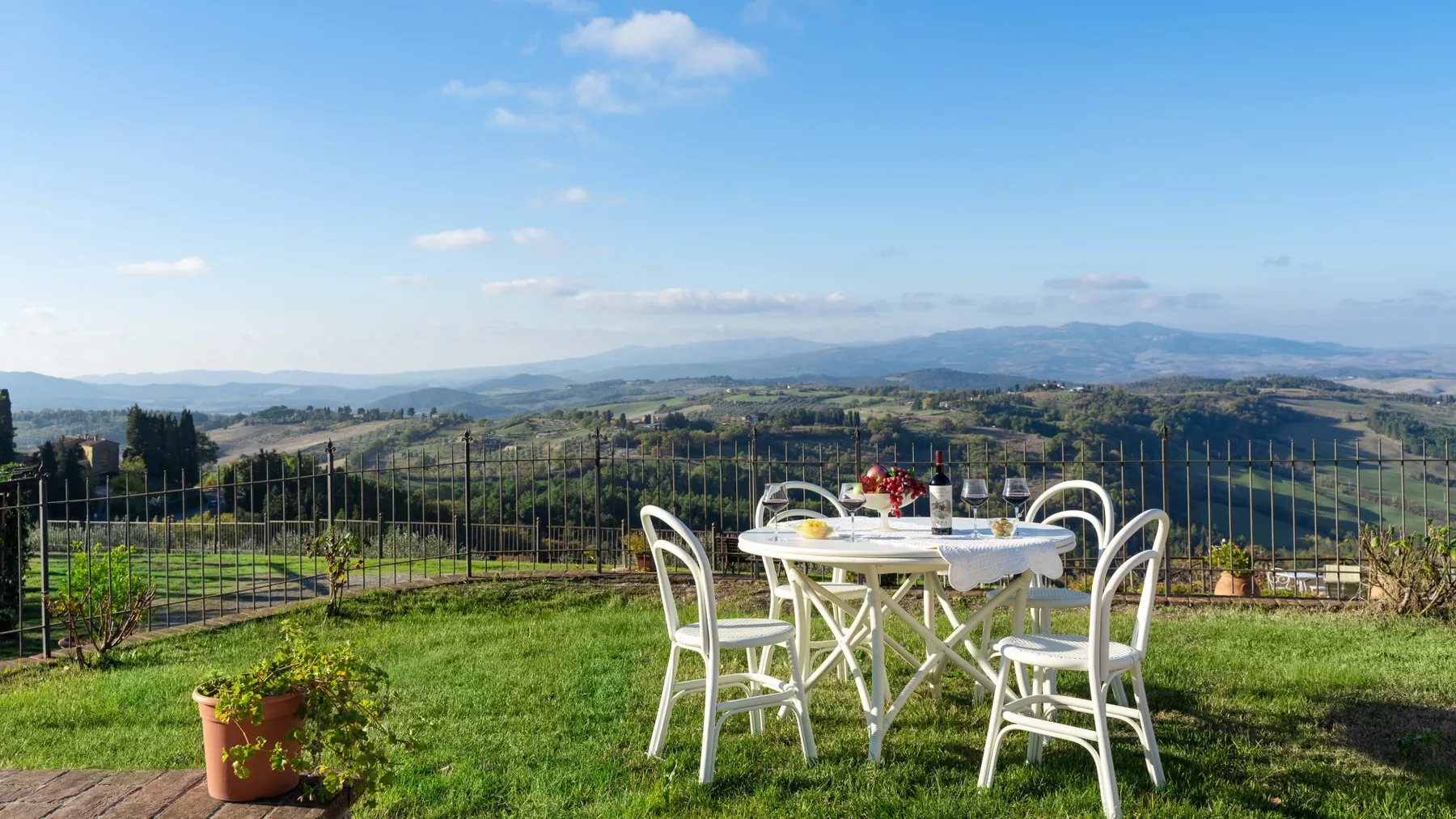 Una mesa y sillas de comedor están en una terraza con césped y vistas a colinas.