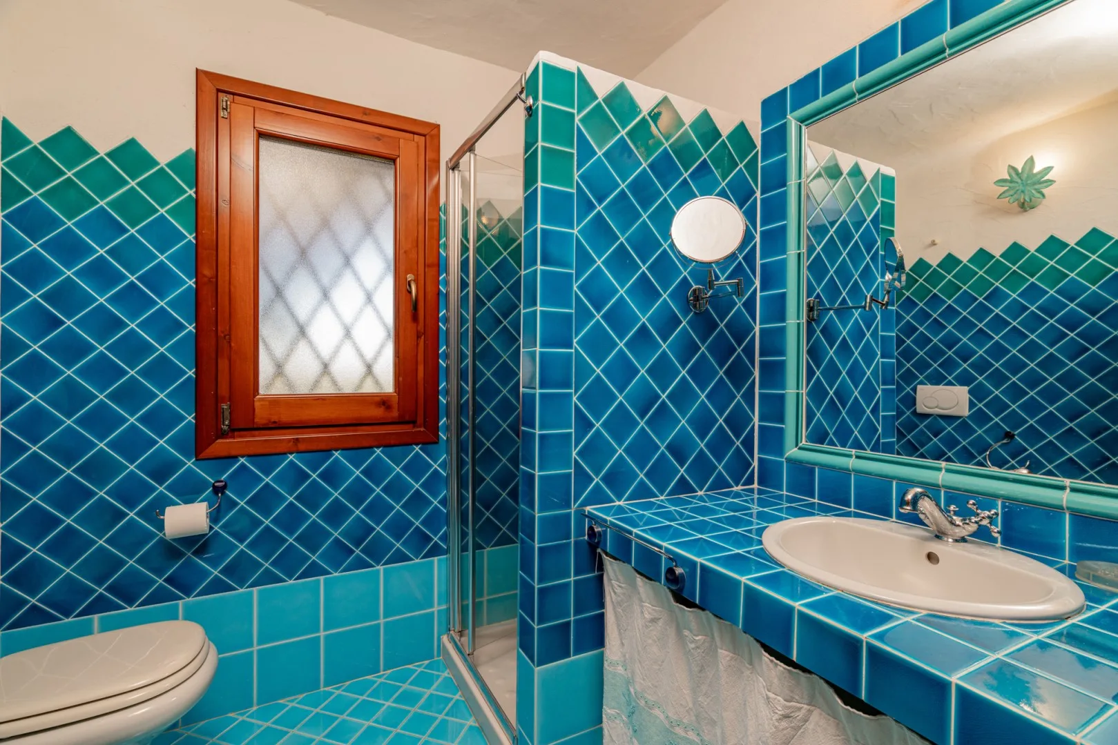 A tiled bathroom with a sink, mirror, shower, and window.