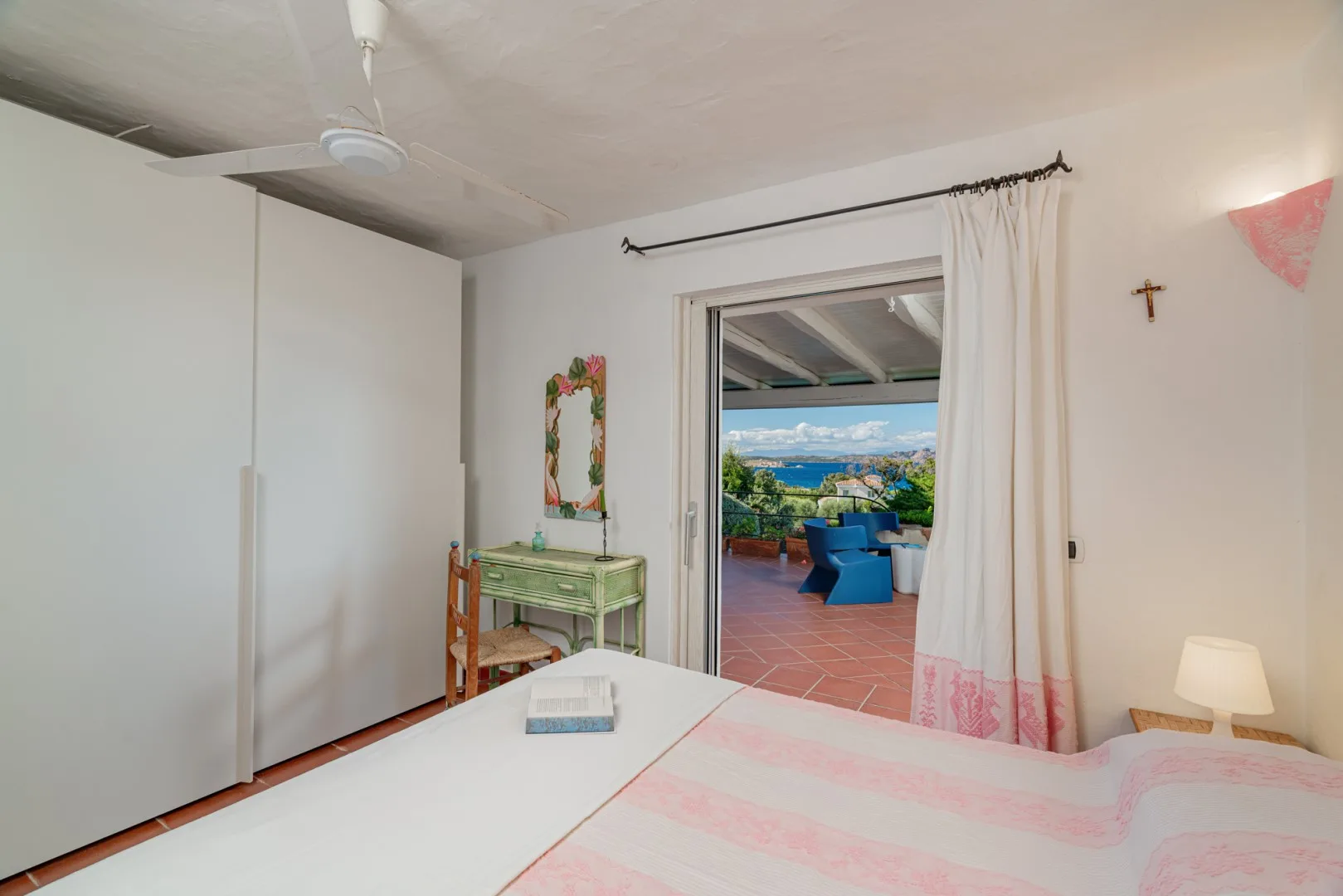 A bedroom with a bed and an open doorway leading to a terrace with seating.