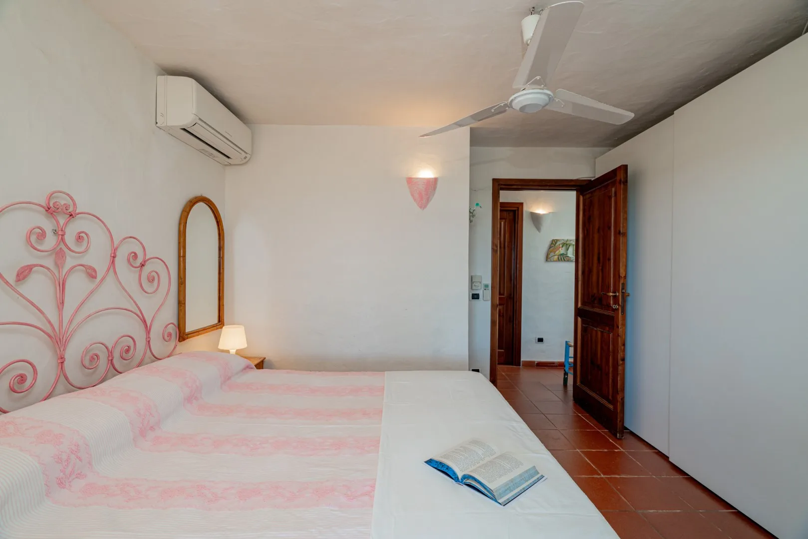 A bedroom with pink-patterned bedding, an open wooden doorway, and a ceiling fan.