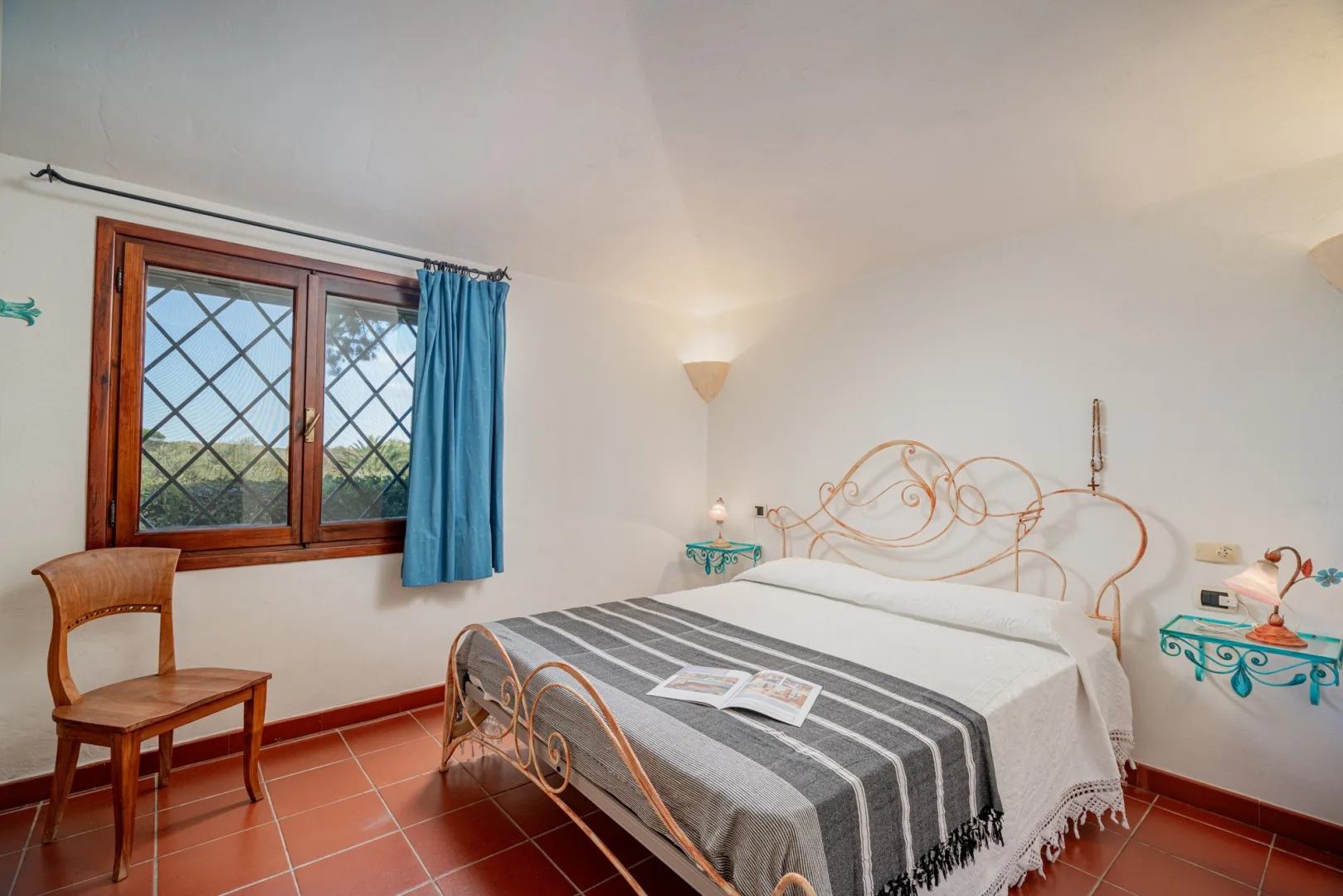 A bedroom with a double bed, gray striped bedding, and a window with blue curtains.