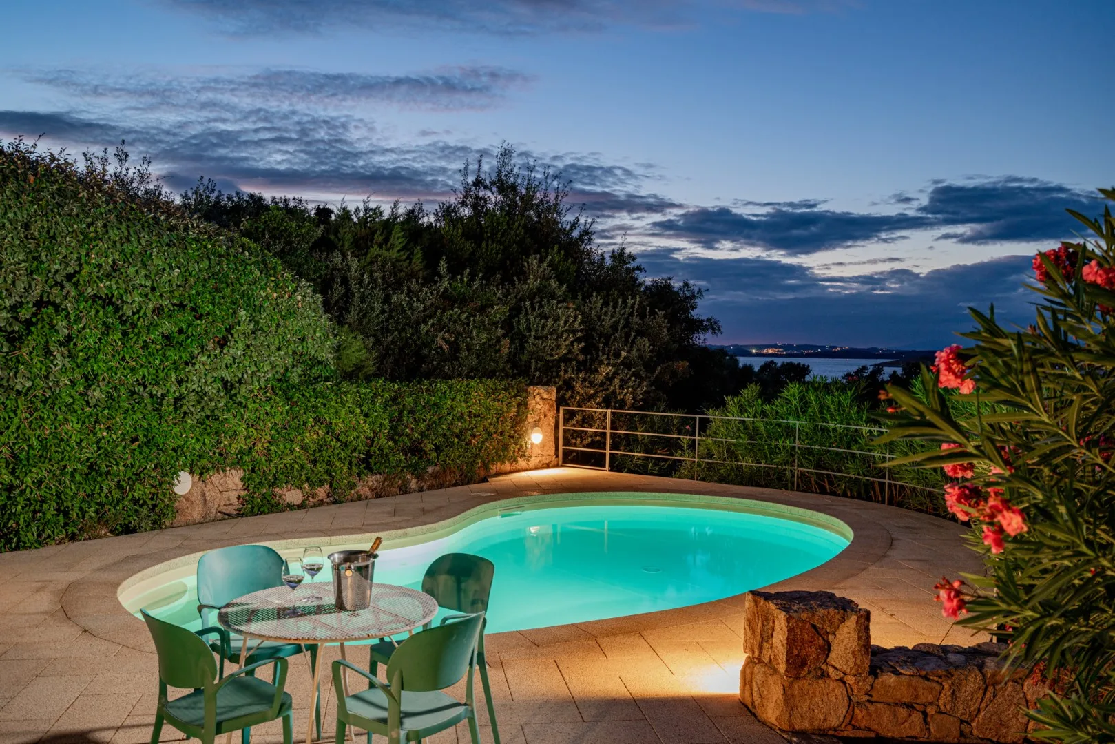 An outdoor swimming pool glows beside a patio seating area at dusk.