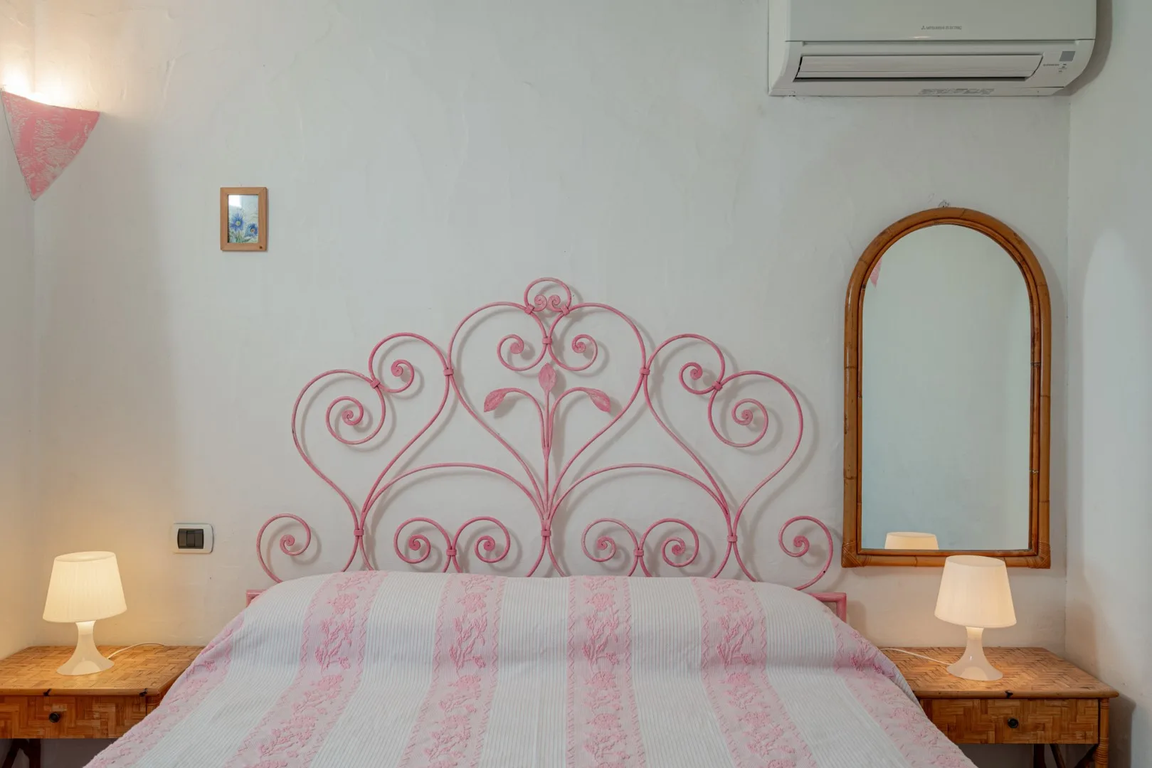A bedroom with a bed, pink metal headboard, and matching bedside tables.