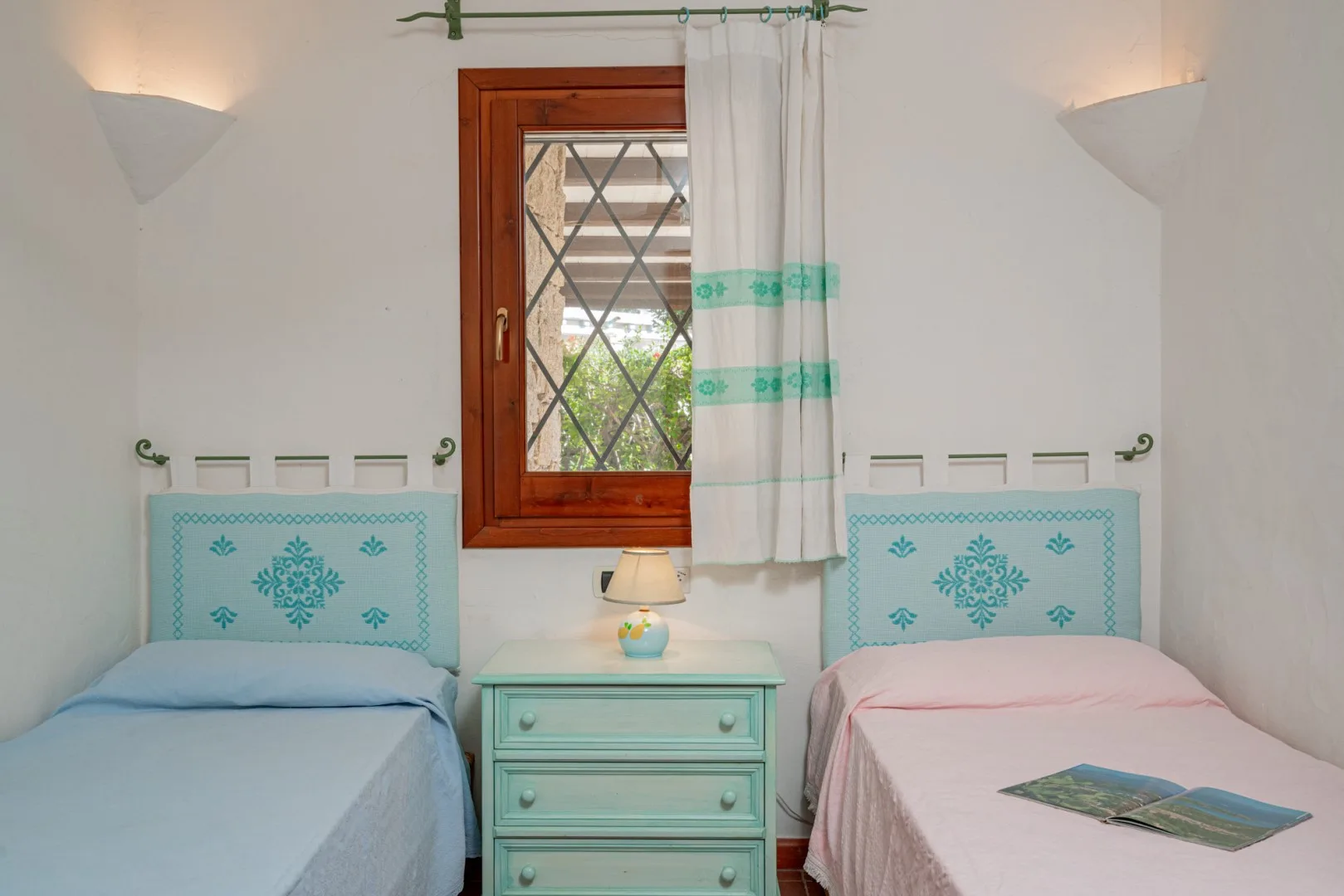 A bedroom with two single beds and a window between them.