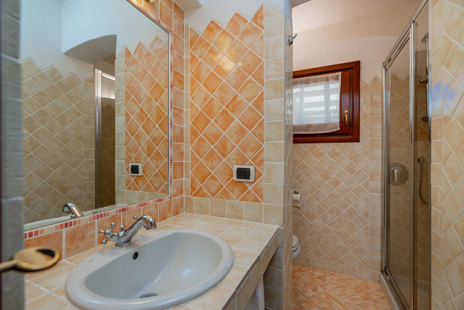 A tiled bathroom with a sink, mirror, and glass shower.