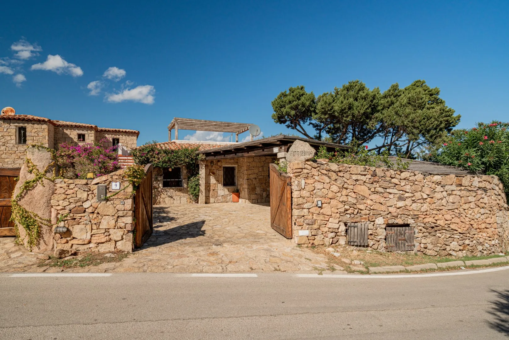 A stone-walled entrance opens onto a courtyard, with trees behind the buildings.