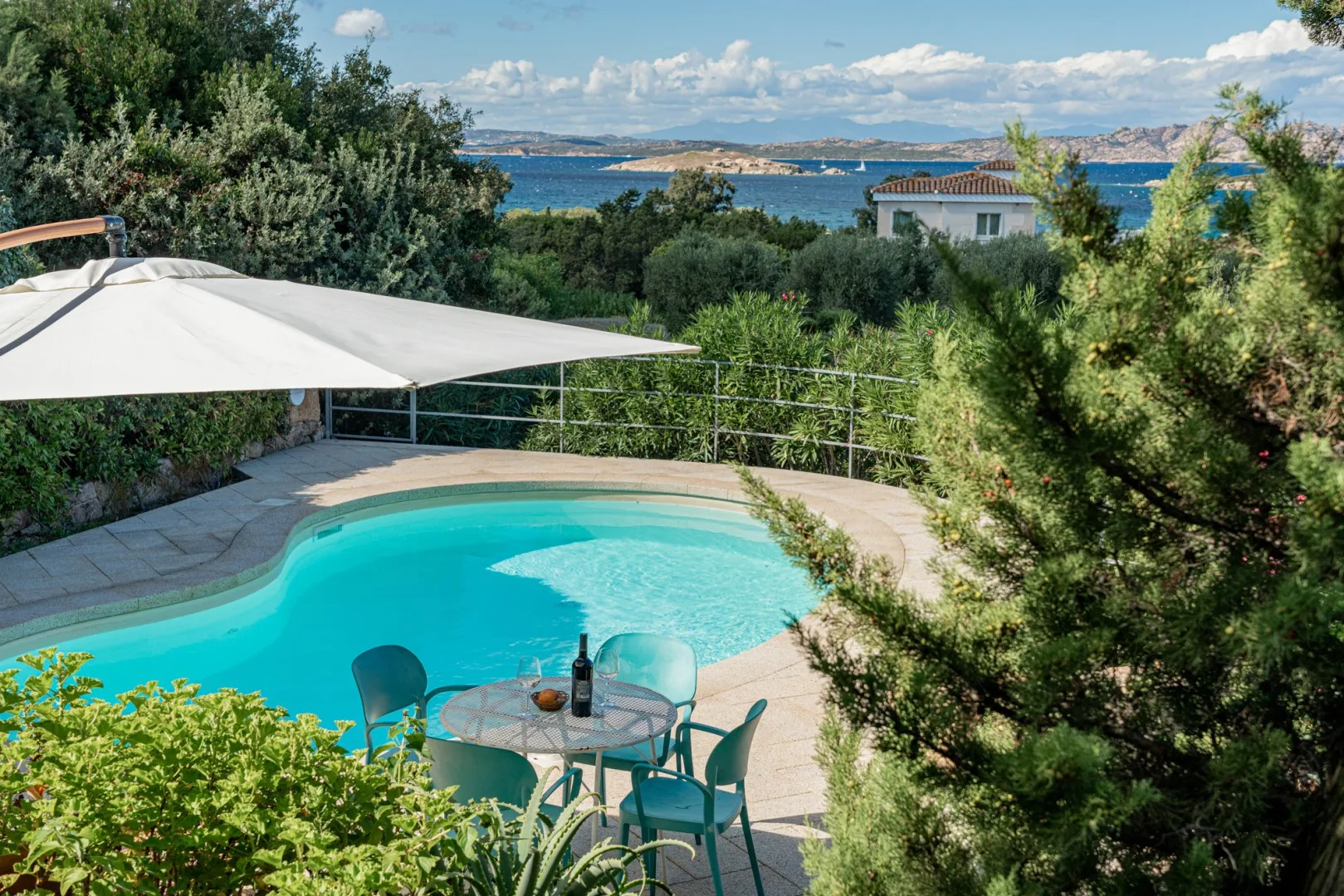 A swimming pool with patio seating overlooks a blue bay.