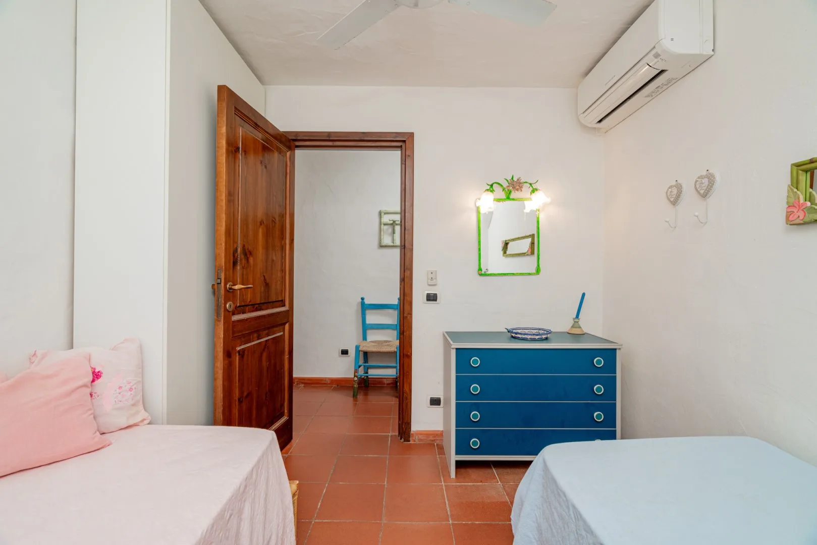 A bedroom with two beds and a blue dresser beneath a wall mirror.
