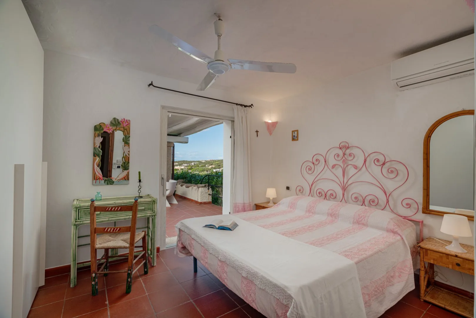 A bedroom with a pink-patterned bed and an open doorway to a terrace.