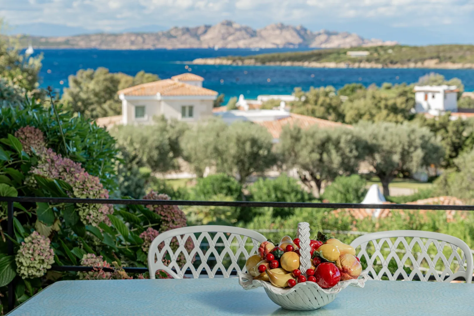 A seaside terrace with a table and a bowl of fruit overlooking the water.