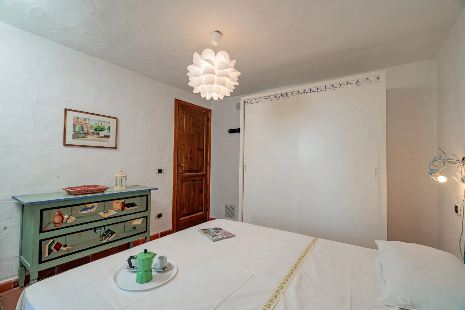 A bedroom with a bed, a wooden door, and a painted dresser.