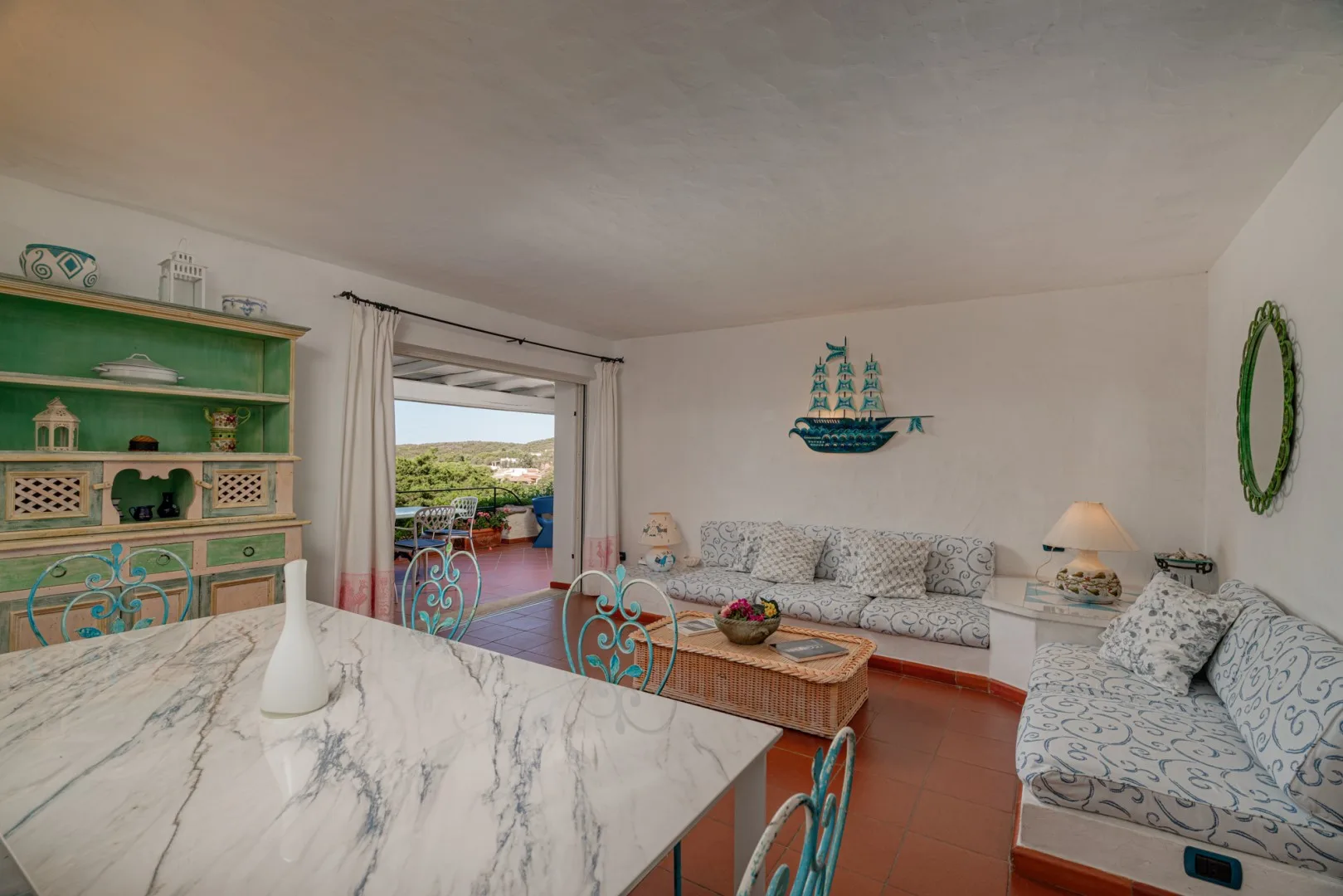 A living and dining area with patterned seating and a table beside an open patio doorway.