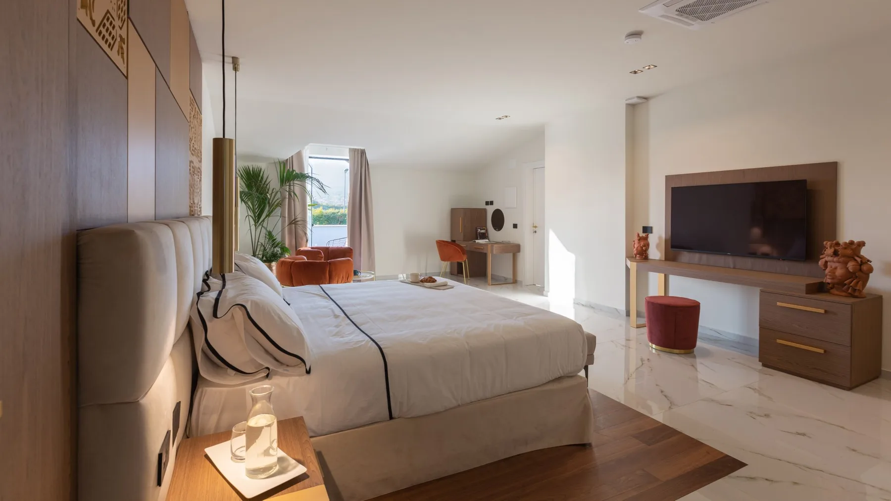 Un dormitorio con una cama grande frente a un televisor y una pequeña zona de estar junto a la ventana.