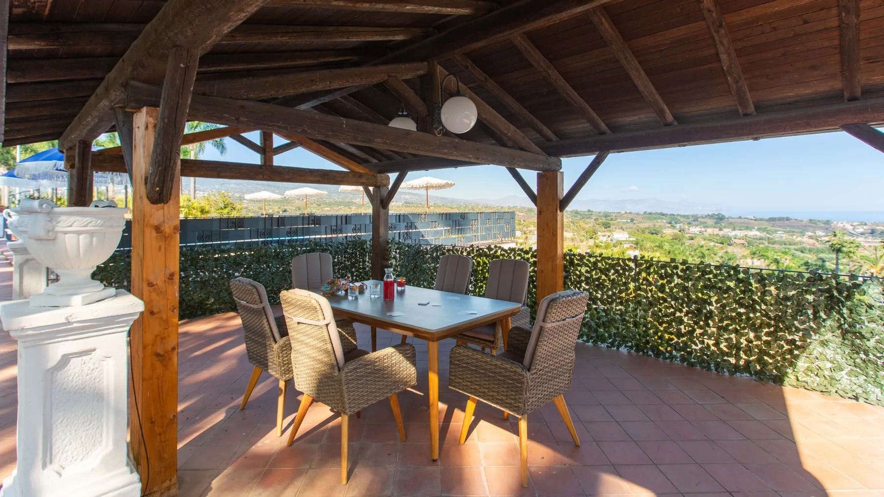 Una zona de comedor exterior cubierta con mesa y asientos tejidos da a un paisaje verde.
