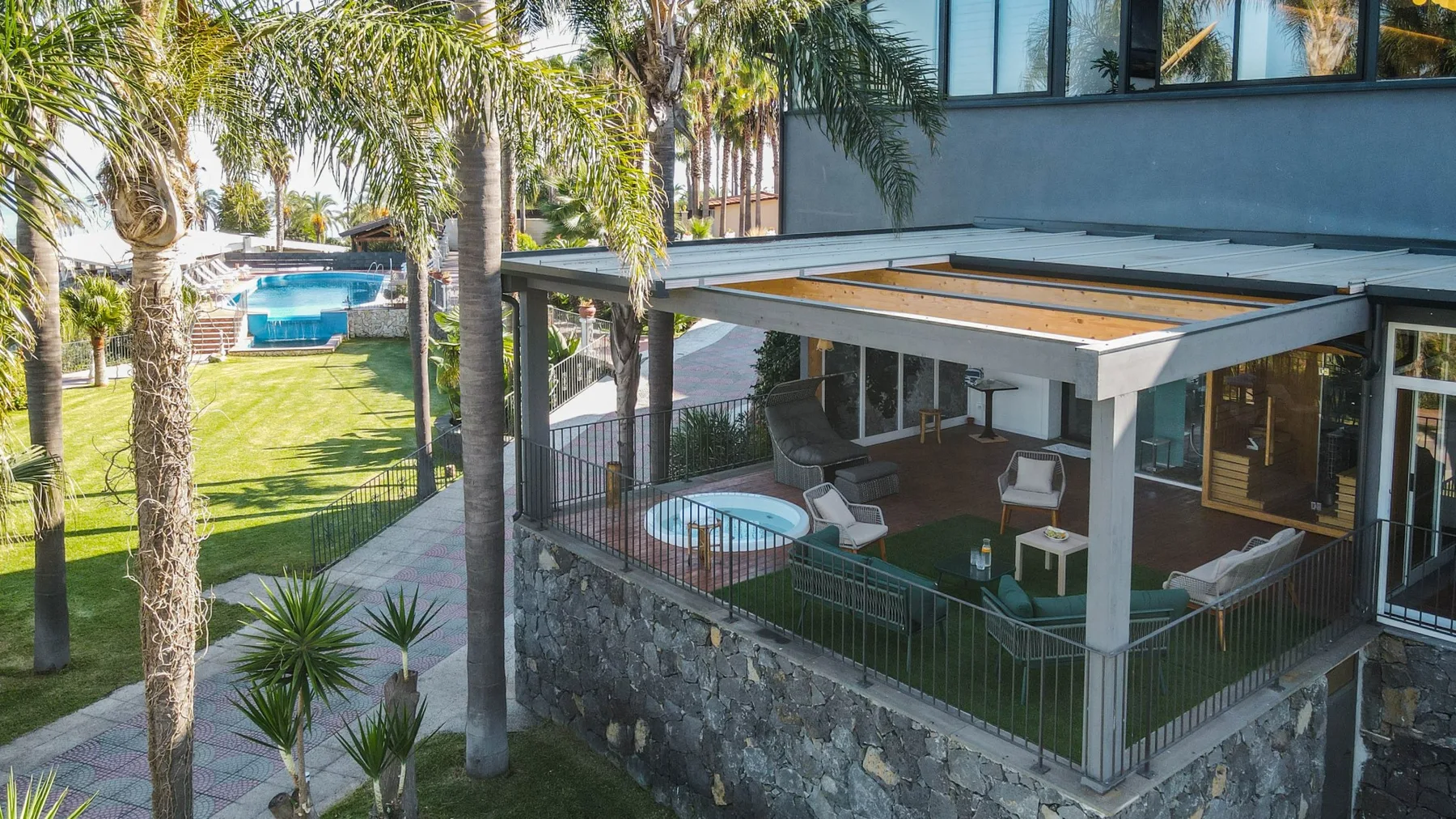 Una casa moderna tiene un patio cubierto con vista al césped, palmeras y una piscina.
