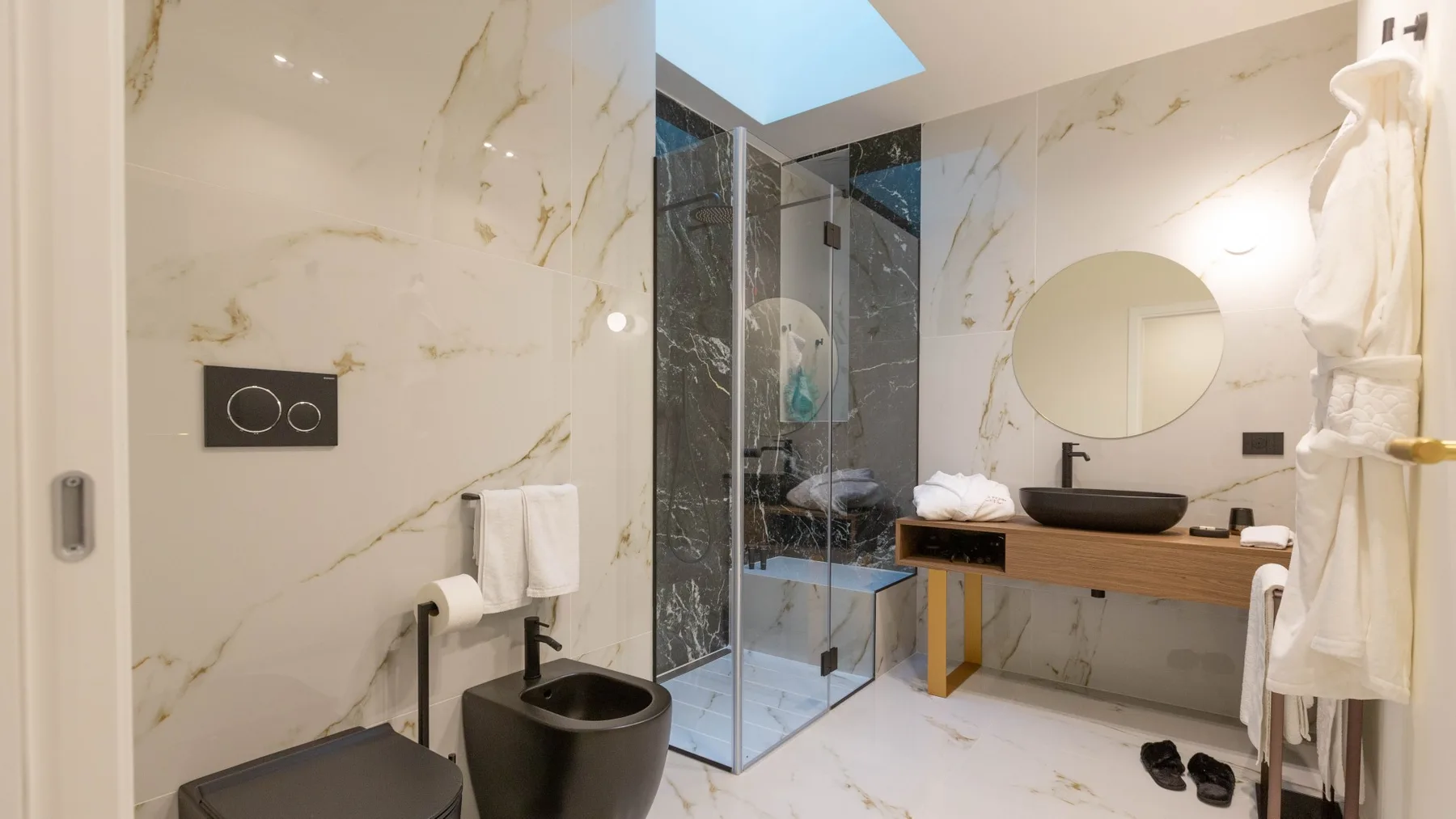 Un baño luminoso con ducha de cristal, inodoro oscuro y lavabo sobre un mueble de madera.
