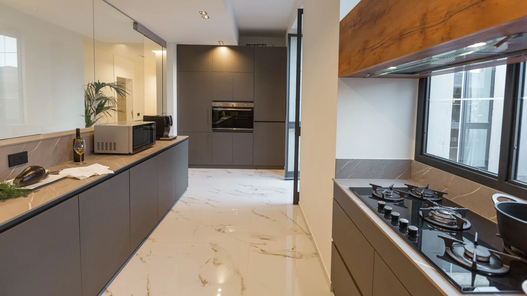 Una cocina moderna con una encimera larga y una placa de cocción junto a grandes ventanas.
