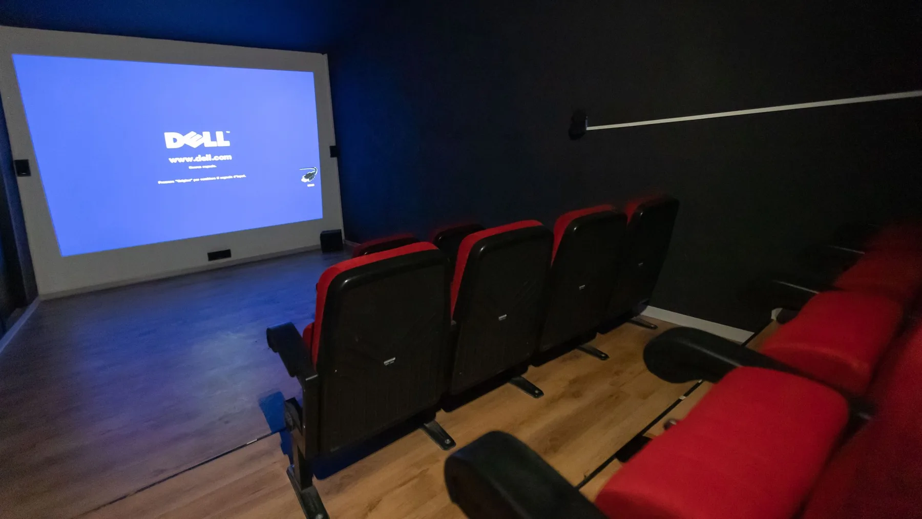 Una pequeña sala de proyección con filas de asientos rojos frente a una imagen proyectada.