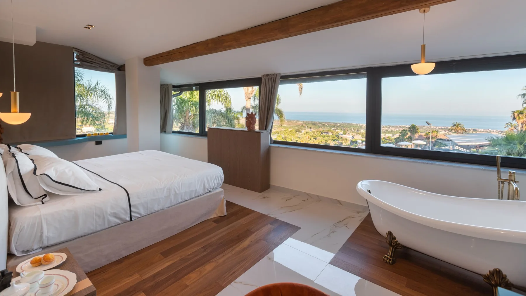 Dormitorio con una cama junto a una bañera exenta y amplias ventanas con vistas al mar.