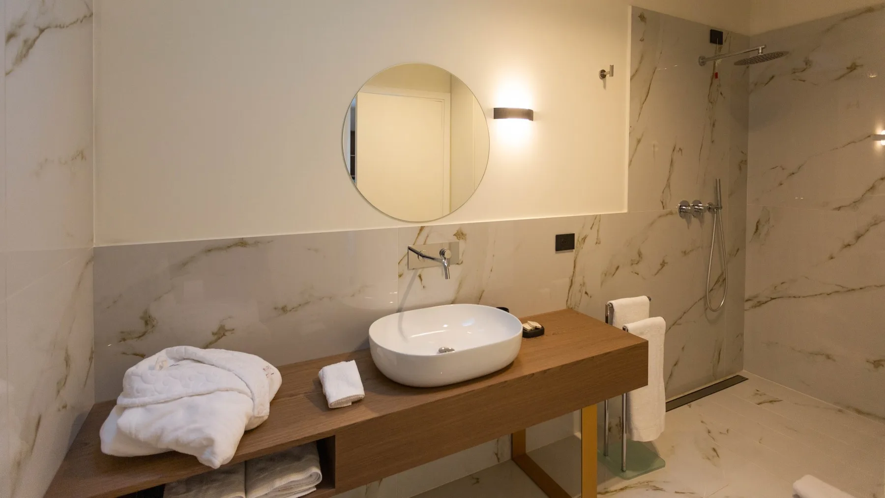 Un lavabo de baño con un espejo redondo y una zona de ducha.