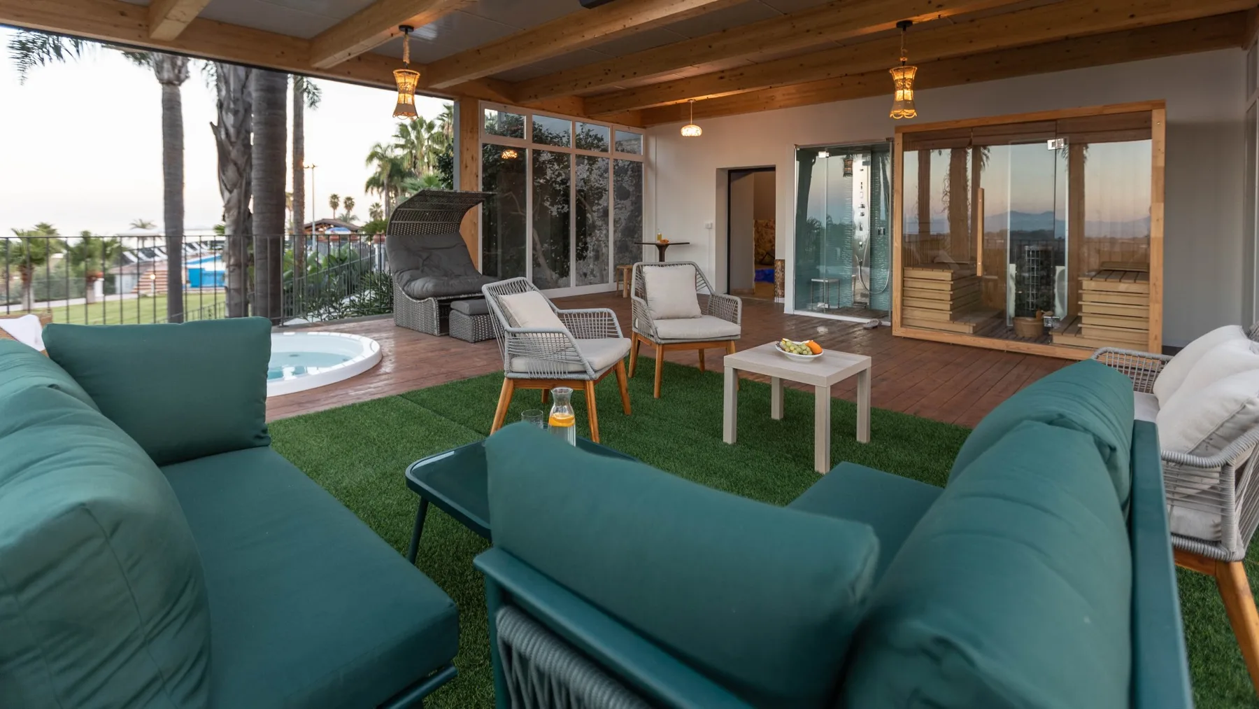 Un patio cubierto tiene asientos color turquesa alrededor de una mesa pequeña, con una piscina a la vista.