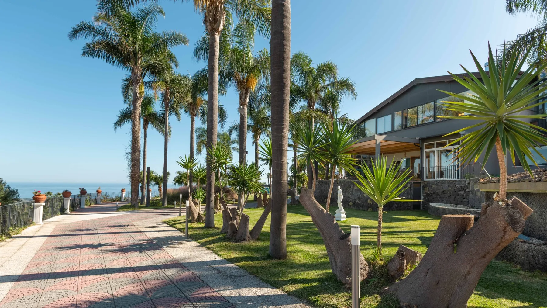 Un camino pavimentado atraviesa un jardín con palmeras junto a un edificio moderno.