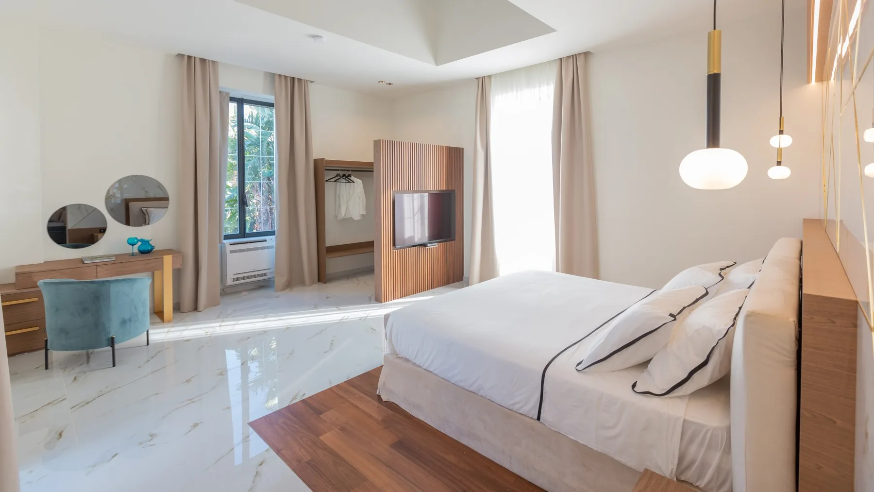 Un dormitorio luminoso con una cama grande, un tocador y ventanas altas.