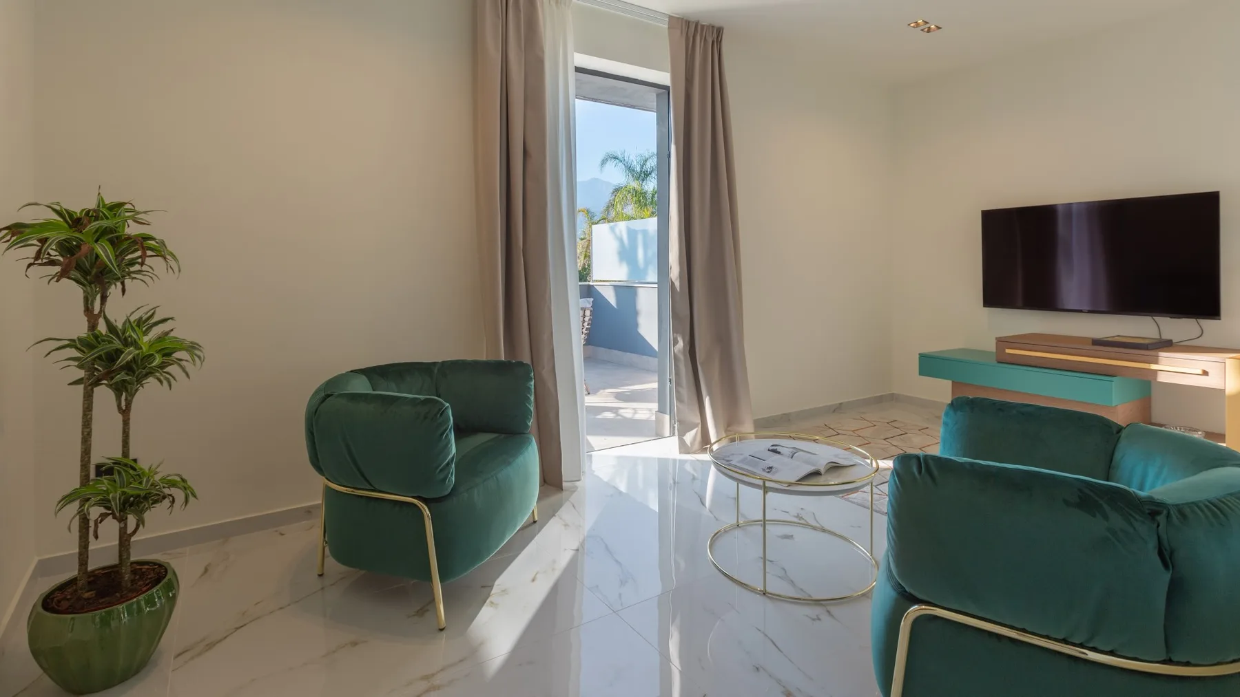 Una sala de estar con asientos verdes, una mesa de centro de vidrio y un televisor.