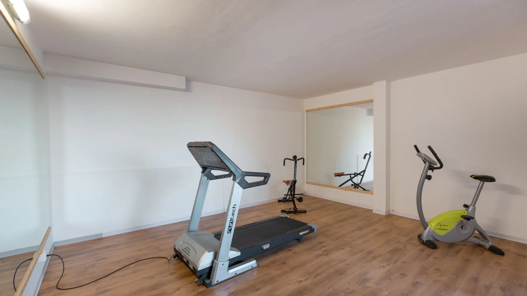 Un gimnasio en casa con equipo de ejercicio sobre un suelo de aspecto madera.