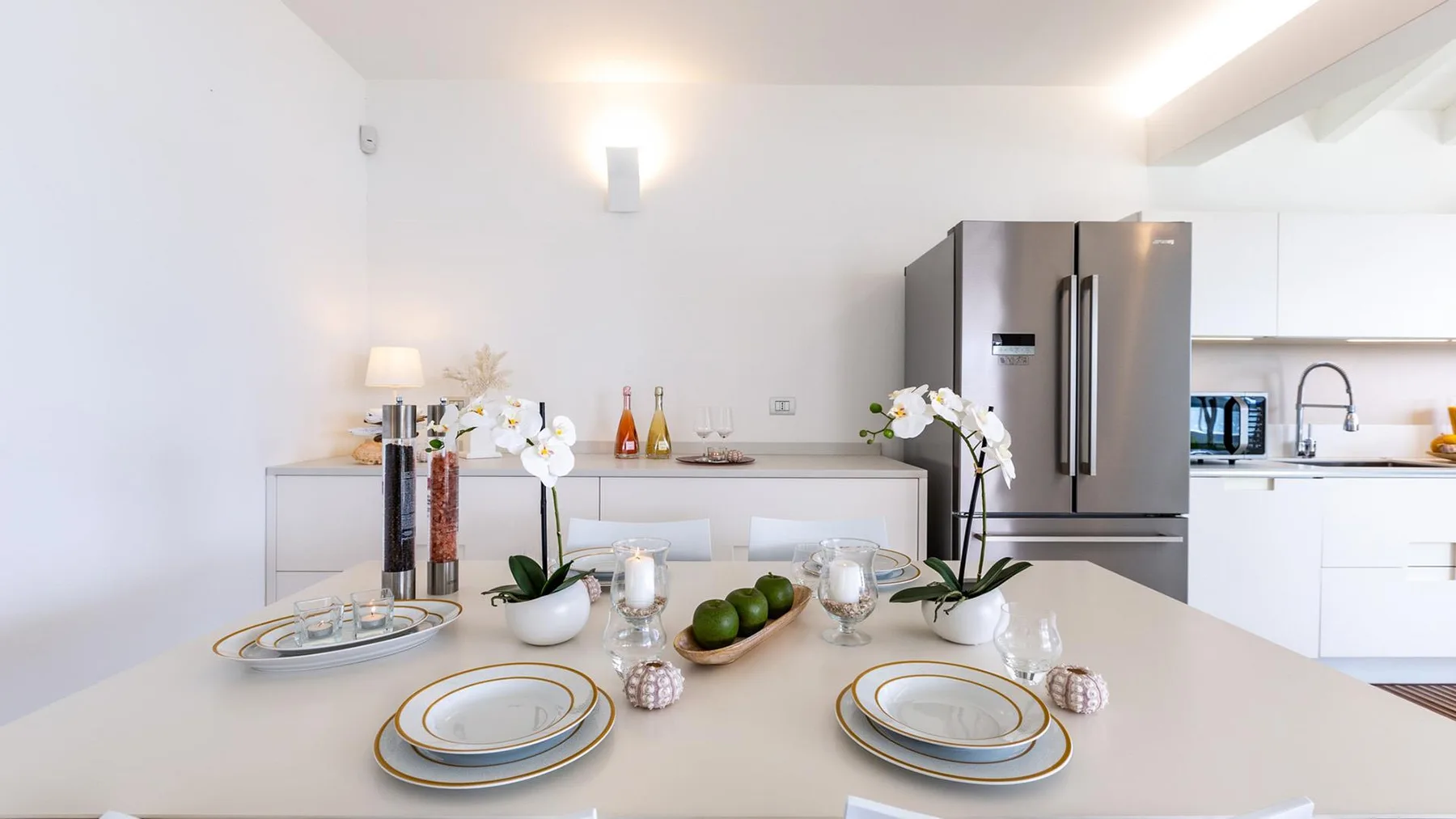 Una mesa de comedor está puesta con platos y flores junto a una cocina luminosa.