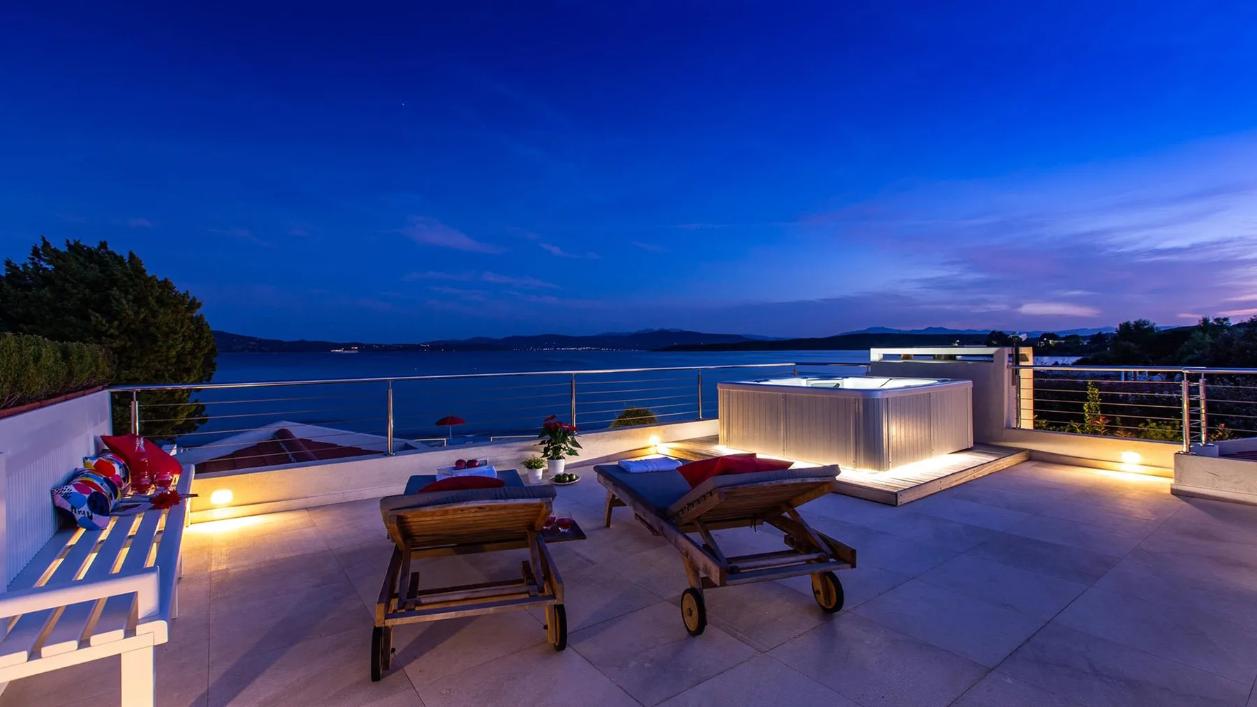 Una terraza en la azotea mira al agua al anochecer, con asientos y luces suaves.
