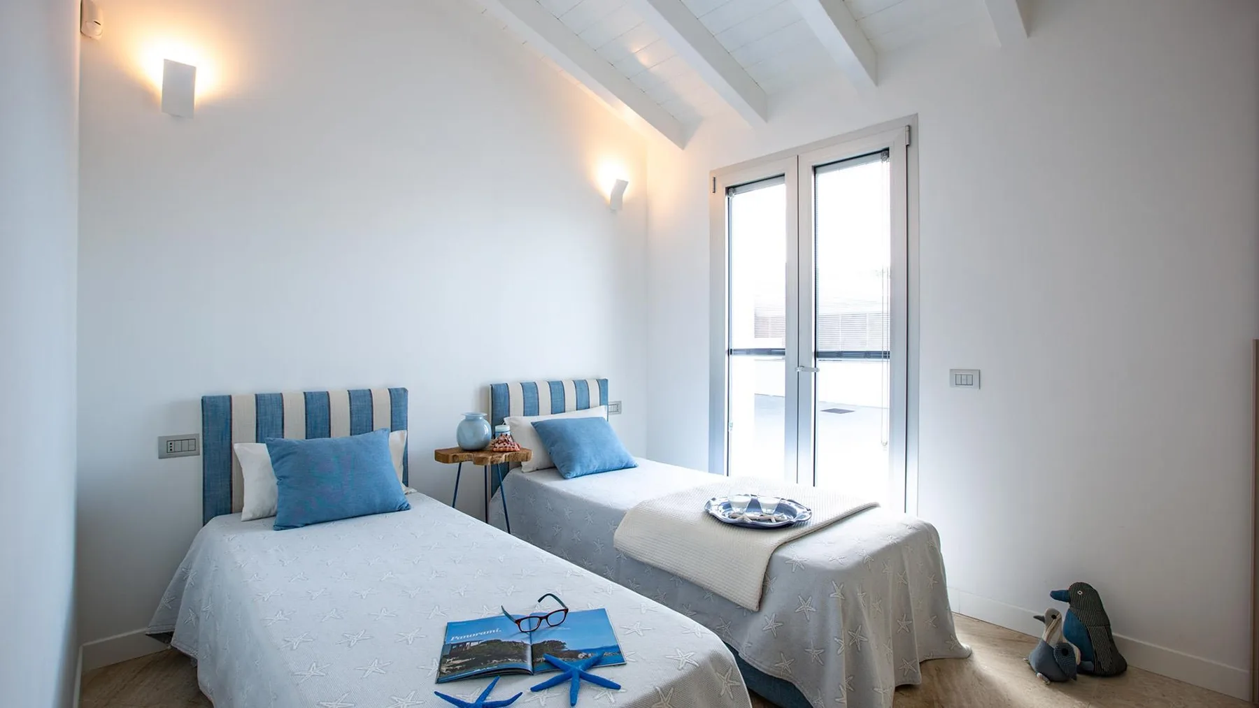 Un dormitorio luminoso con dos camas y puertas de cristal que dan a un balcón.