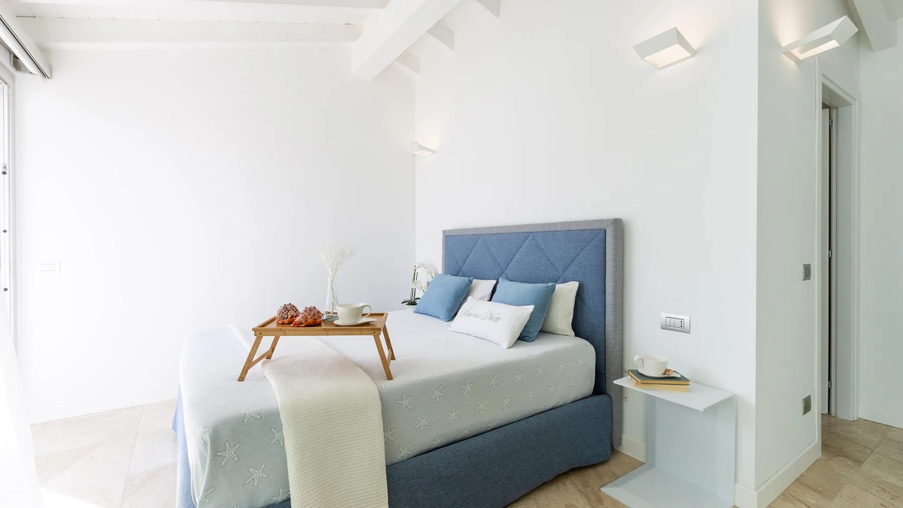 Un dormitorio con una cama, cabecero azul tapizado y una pequeña mesa auxiliar.