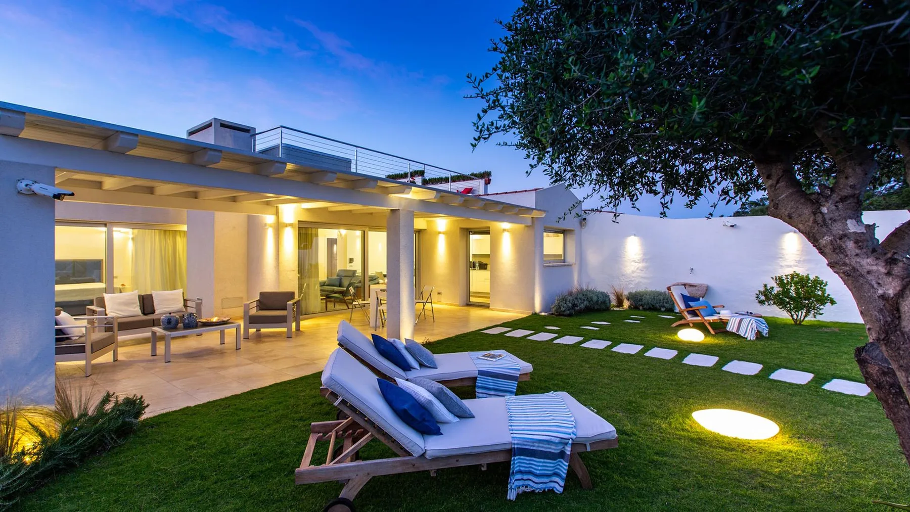 Una casa moderna se abre a un patio con césped, asientos y tumbonas.