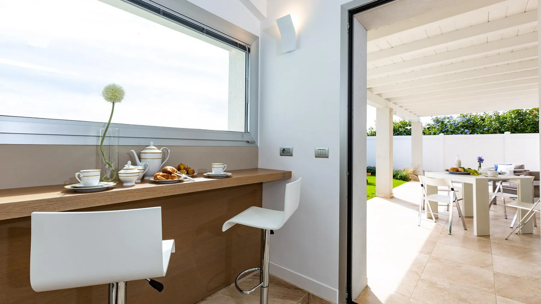 Una luminosa barra de cocina con asientos blancos da a un comedor exterior cubierto.