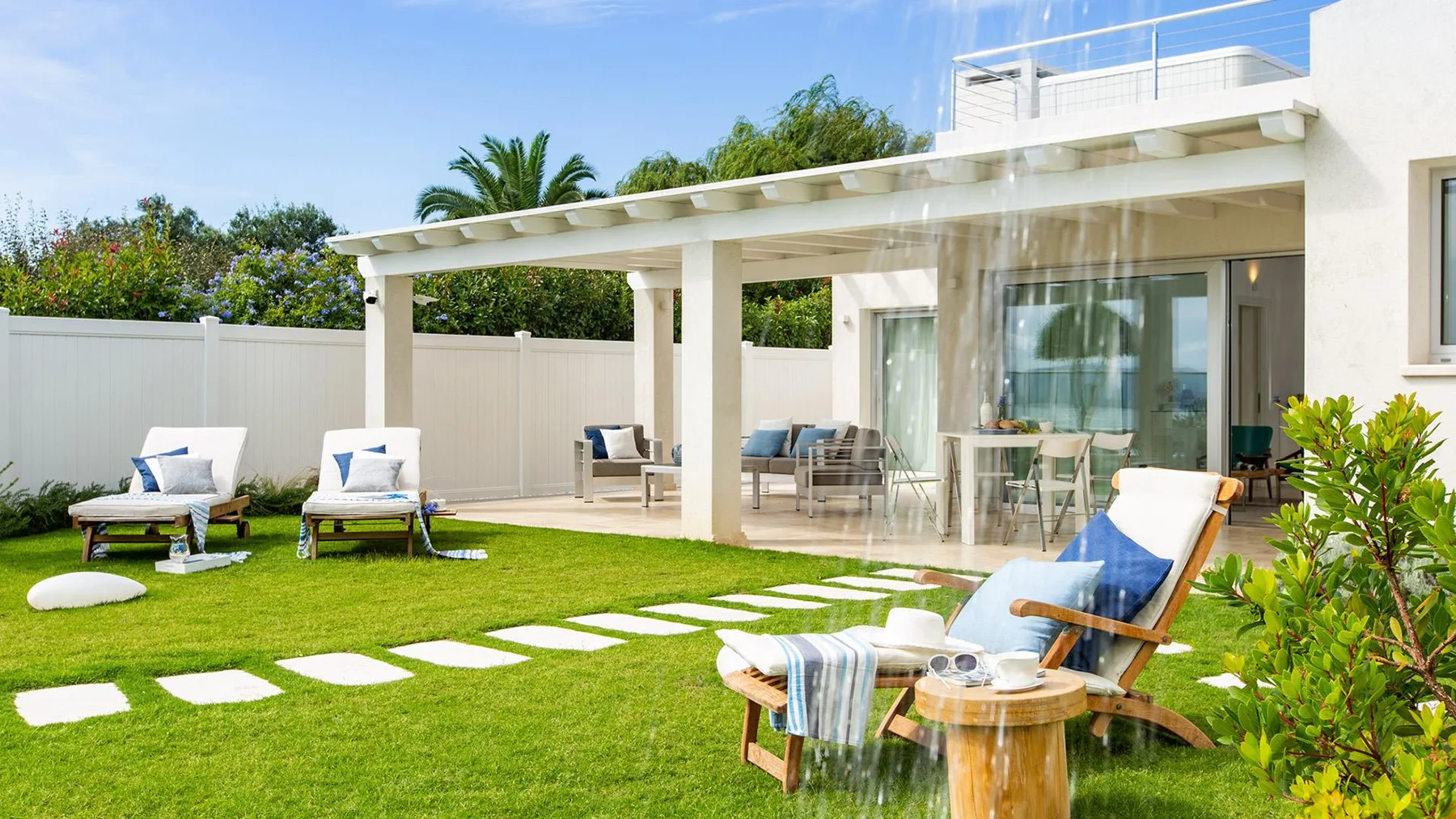 Un patio soleado con asientos al aire libre da a un césped verde junto a la casa.